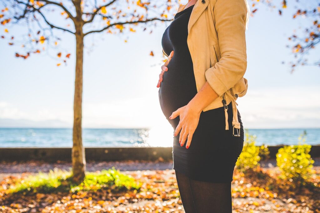 Schwangere Frau im Herbst vor Meer mit Baum